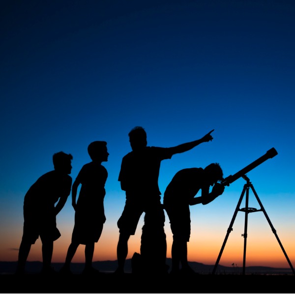 Adulte et enfants observant le ciel à travers une lunette astronomique