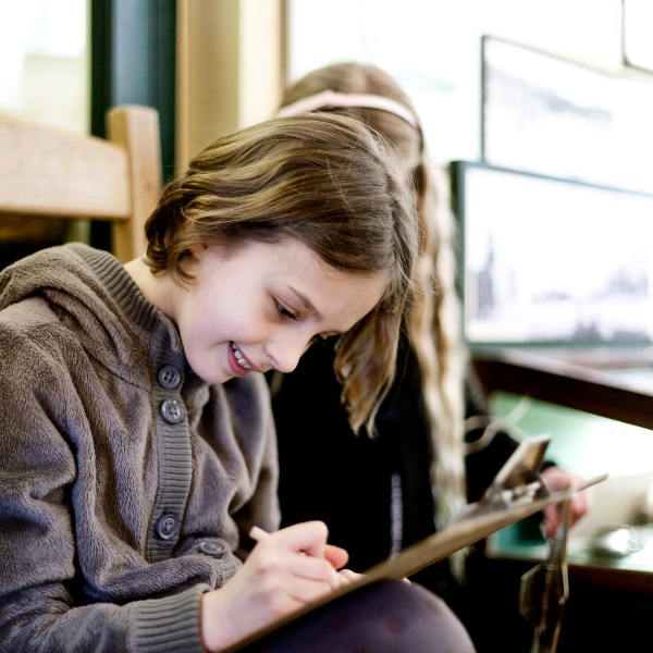 Une fille écrit des notes sur un presse-papiers avec une autre fille derrière elle.