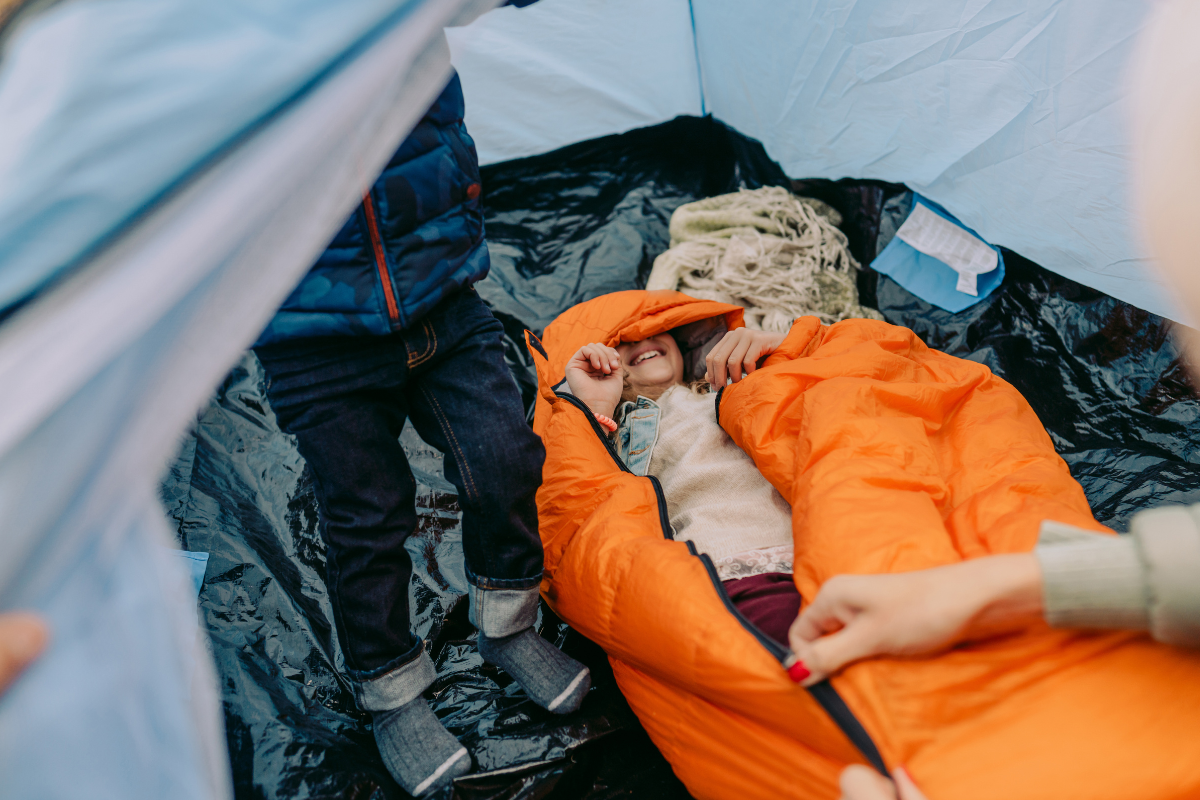 Un enfant souriant dans un sac de couchage, dans une tente