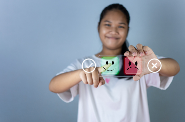 Shown is a colour photograph of a young person touching a happy face icon on a clear tablet.