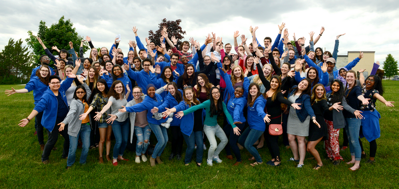 Un grand groupe de bénévoles de Let's Talk Science pose ensemble à l'extérieur, souriant, les bras tendus.