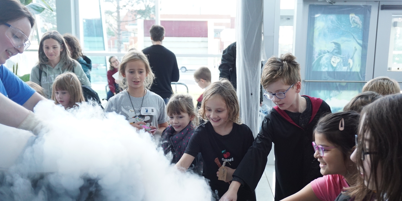 Des enfants s'émerveillent lors d'une activité scientifique et tendent la main pour toucher de la glace sèche lors de l'événement de Parlons sciences «School of Witchcraft and Wizardry » à l'Université Memorial de Terre-Neuve.