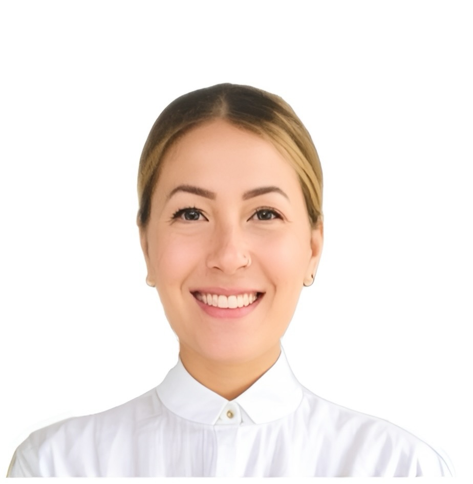 Photo couleur représentant le portrait d’une femme. Elle a les cheveux clairs et ils sont attachés à l’arrière. Elle sourit, vêtue d’un chemisier blanc boutonné jusqu’au cou. L’arrière-plan est blanc.