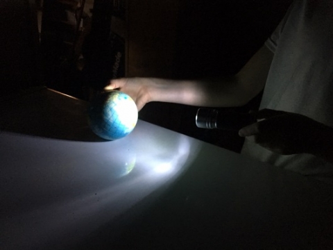 Image d’un élève éclairant de sa lampe de poche un globe terrestre