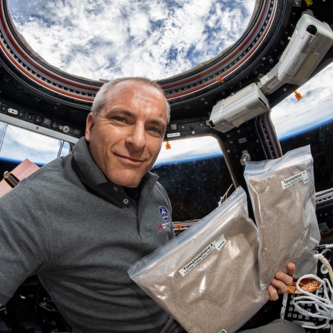  L’astronaute canadien David Saint-Jacques tient des semences de Tomatosphère à bord de la Station spatiale internationale. On aperçoit la Terre au loin.