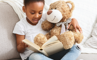 Young black child reads a book with a teddy bear
