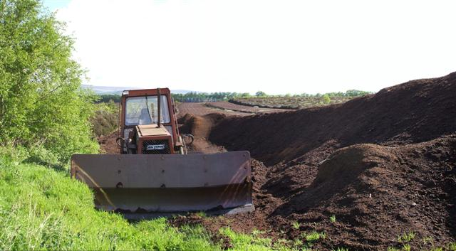 Shown is a colour photograph of a tractor beside a large pile of peat soil.