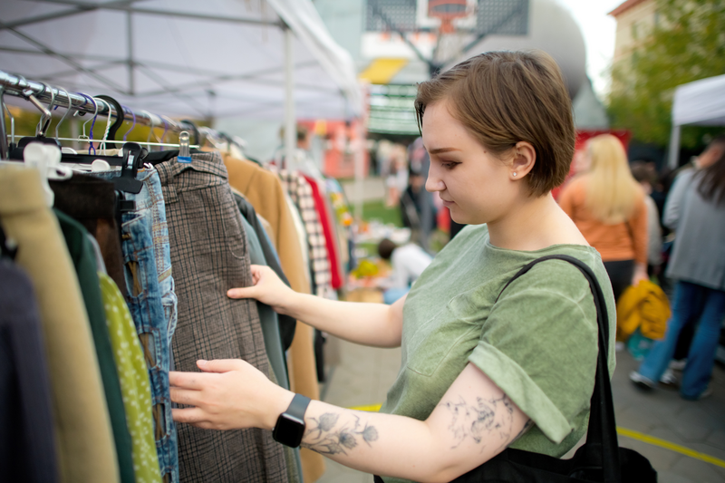 Young woman choosing second hand clothes at a flea market. 