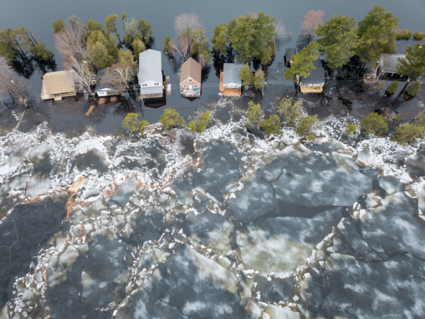 Une photographie aérienne en couleur montre une rangée de maisons entourées d’eau.