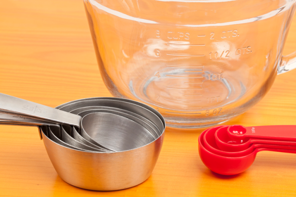 Shown is a colour photograph of a liquid measuring cup, dry measuring cups and measuring spoons, on a wooden table.