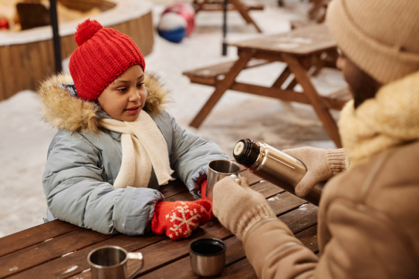 Shown is a colour photograph of an adult and a child sharing a warm drink on a cold day.