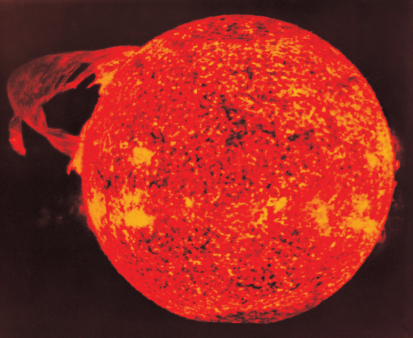 Shown is a colour photograph of a glowing red loop stretching out from the Sun’s surface.
