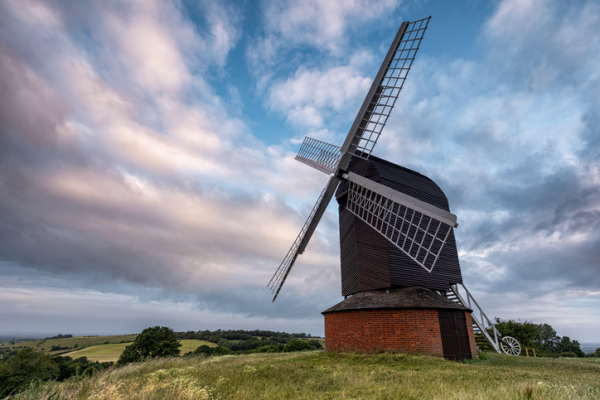Shown is a colour photograph of a windmill on top of a hill.