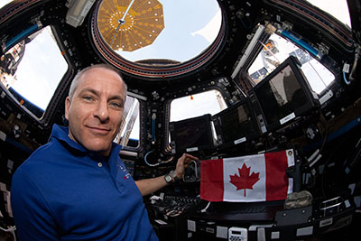 
			L'astronaute David Saint-Jacques à bord de la Station spatiale internationale avec un drapeau du Canada